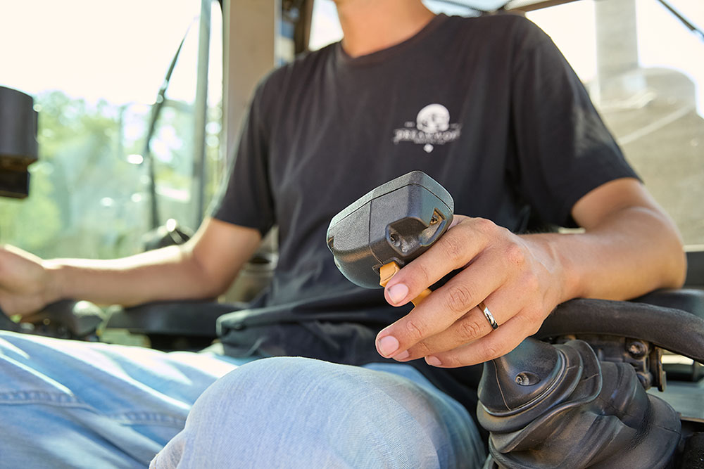 Close-up of a man, Nick Castillion, sitting in an equipment cab, holding a black control joystick with his left hand, wearing a black T-shirt and jeans.